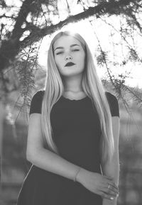 Portrait of a beautiful young woman standing against trees