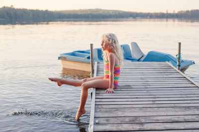 Side view of girl sitting on pier by lake