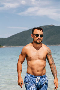 Portrait of young man standing at beach against sky