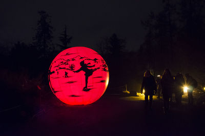 Silhouette people walking against illuminated trees at night