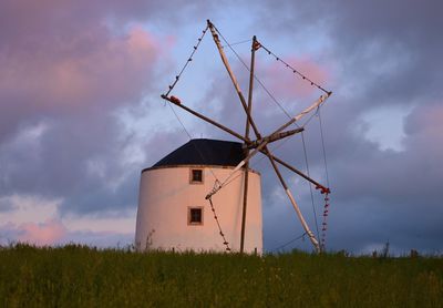 Traditional windmill on grassy field against sky during sunset