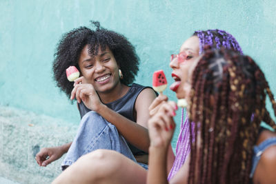 Female friends eating flavored ice while sitting outdoors