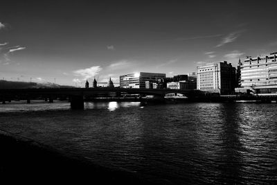 Bridge over river by buildings in city against sky