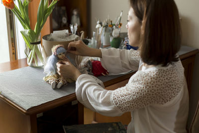Woman decorating handmade doll on table at home