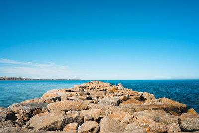 Rocks on shore by sea against blue sky