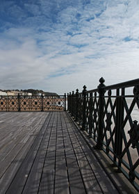 Empty footbridge against cloudy sky