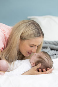 Mother kissing baby girl on bed at home
