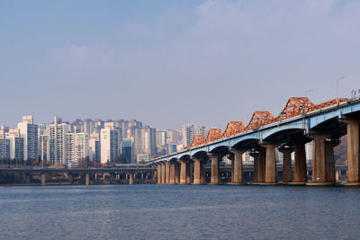 Bridge over river by buildings against sky in city