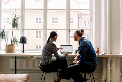 Female executive pointing on laptop while discussing with colleague in office