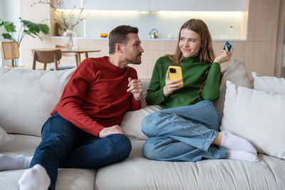 Family couple young man woman buying online in smartphone sitting on couch at home.
