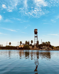 Water tower by lake against sky