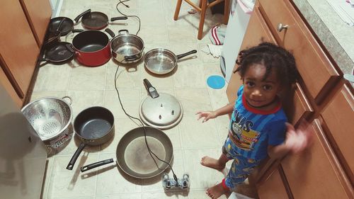 Full length portrait of boy standing by utensils on floor in kitchen