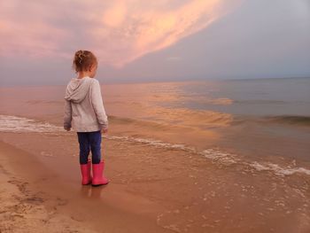 Girl standing at beach against sky during sunset