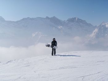 Snowboarder standing against snowcapped mountains