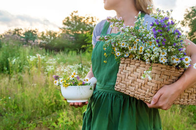 Midsection of woman holding flowers in mortar and basket in farm