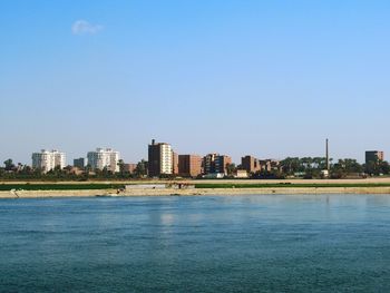 Sea by buildings against clear blue sky