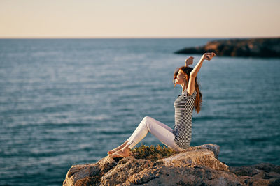 Young woman on rock by sea against sky