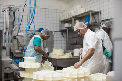 Cheese factory workers cleaning containers with hose