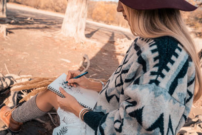 Midsection of woman holding hat while sitting outdoors