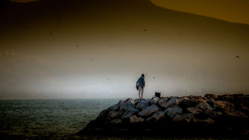 Man standing on rock by sea against sky