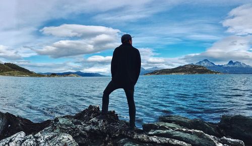 Rear view of man standing on rock by sea against sky