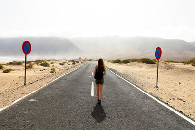 Rear view of woman walking on road against sky