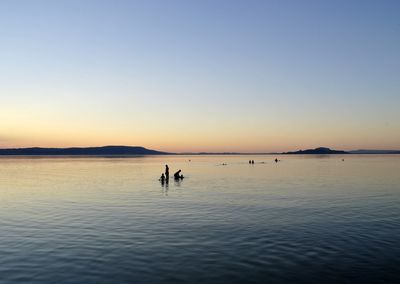 Silhouette people in sea against clear sky during sunset