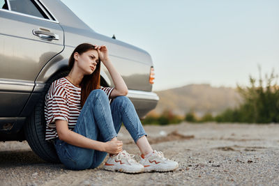 Portrait of young woman sitting on car