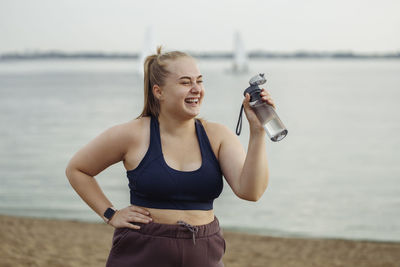 Happy young woman standing with water bottle on beach