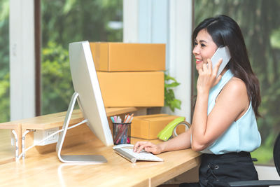 Side view of young woman using phone while sitting on table