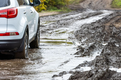 Clean white suv car moving on a dirt road with wet clay in front of the blurry slope