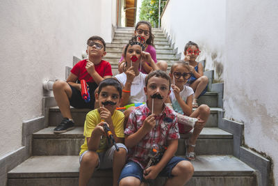 Group of little boys of different ages sitting on a stairway playing together with fun accessories