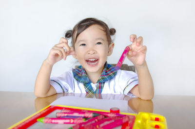 Portrait of smiling girl holding crayons on table