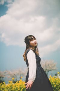 Side view of young woman standing against sky