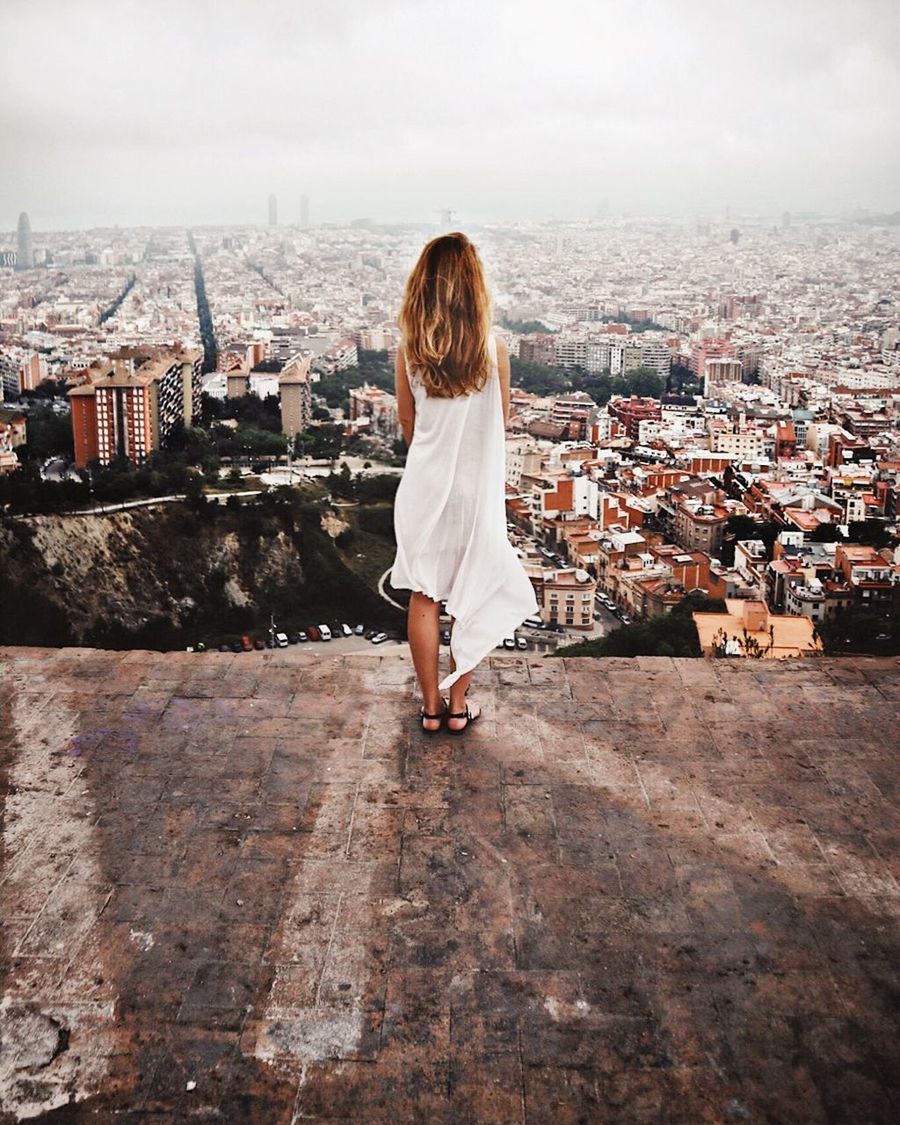 REAR VIEW OF WOMAN STANDING BY BUILDINGS AGAINST SKY