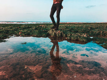 Low section of man standing on rock by water