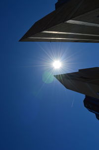 Low angle view of sun shining over clear blue sky