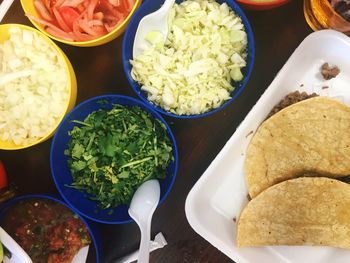 Directly above shot of tacos with chopped vegetables in bowl on table