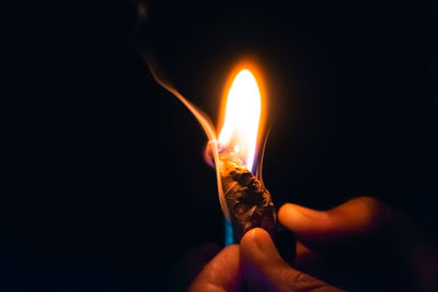 Close-up of hand holding lit candle in the dark