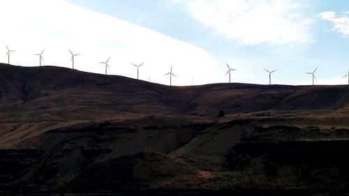Low angle view of windmills on field against sky