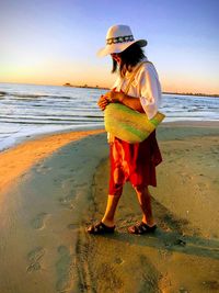 Side view of woman walking at beach against sky during sunset