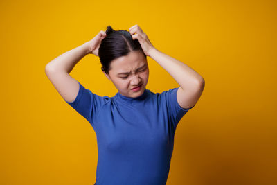 Young woman standing against yellow background