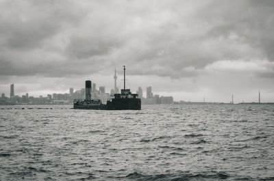 Ship sailing in sea against cloudy sky