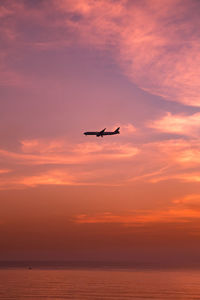 Airplane flying over sea against sky during sunset