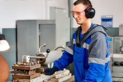 Young turner in safety glasses and headphones works at lathe in workshop. authentic scene workflow