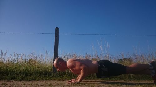 Full length of shirtless man exercising on field against blue sky