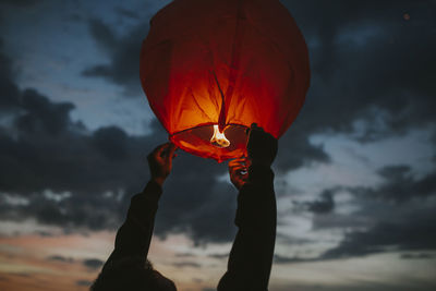 Cropped hands of person holding lantern against sky