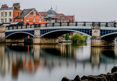 Bridge over river by buildings against sky in city