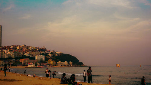 People at beach against sky during sunset