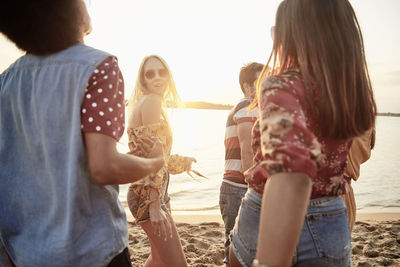 Friends enjoying at beach against sky